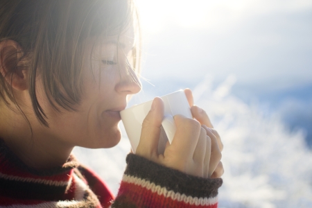 Beautiful young woman drinking hot drink outside on a sunny cold winter morningの写真素材