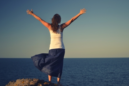 Beautiful young woman standing on a rock greeting the sea.の写真素材