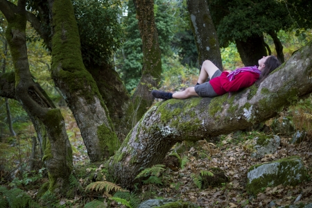 Beautiful young woman wearing sports outfit sitting on a tree trunk enjoying the tranquility of an old natural forest on the island of Thassos, Greece.の写真素材