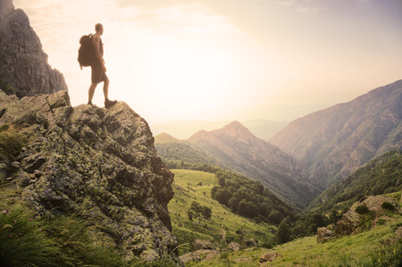 Healthy young man standing on top of a rock high in the mountains, enjoying the natural beauty in the morning light.