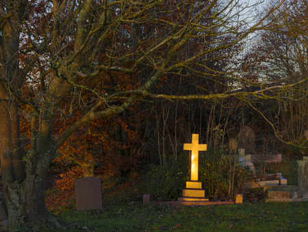 The golden light of the setting sun shining upon a gravestone cross in a cemetery in England, United Kingdomの写真素材