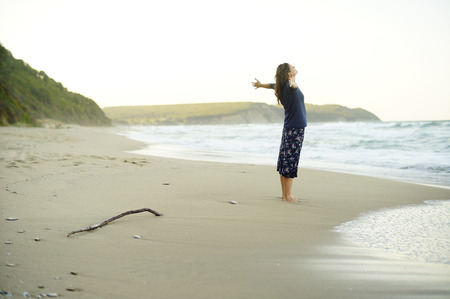 Beautiful young woman with her arms up enjoying the sense of freedom on a desolate beach.の写真素材