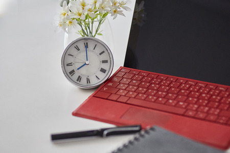 Close up of Clock,red tablet notebook and pen computer on white table. Selective focus