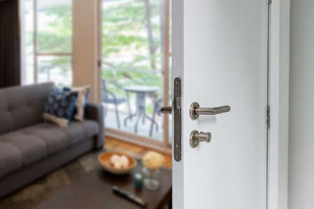Opened wood door to living room and seen outside green view. Half opened Door with handles to living...