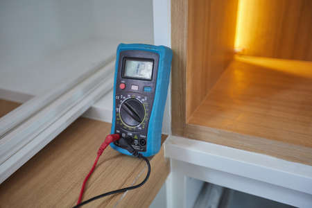 Digital Multi meter on wooden table  in front of lighting in shelf interior. Close up Selective...