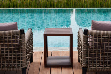 blured table and chairs  in front of blue water swimming pool.   blur table and chairs in forground view of swimming pool.の写真素材
