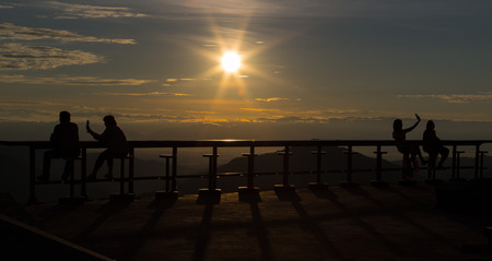 This image is silhouette persons, they are sit on the wooden chairs at the top of mountain on sunrise.のeditorial素材