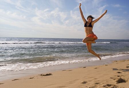 pretty young girl is jumping up in  the air at the beachの写真素材