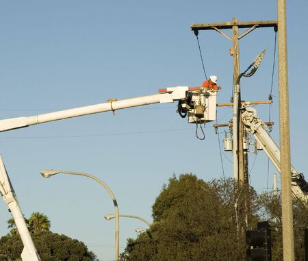 blue collar utility pole worker installing new wires and cables on power utility poleの写真素材