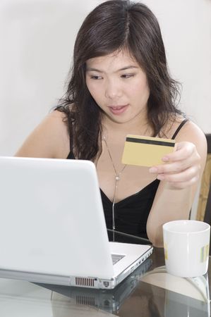 Pretty Asian woman with notebook computer and credit card sitting at tableの写真素材