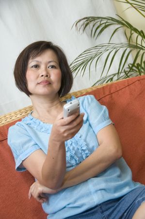 Woman sitting on her sofa with remote control watching televisionの写真素材
