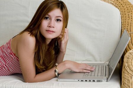 Beautiful young Asian woman laying down and using computerの写真素材