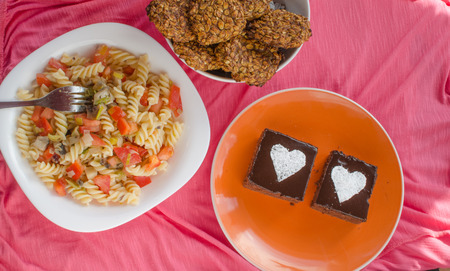 Chocolate cake with heards from sugar on plate,cookies and salad on pink bachgroundの写真素材
