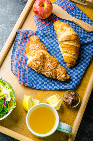 Breakfast in bed on wood tray - apple, croissant, butter, chocolate and saladの写真素材