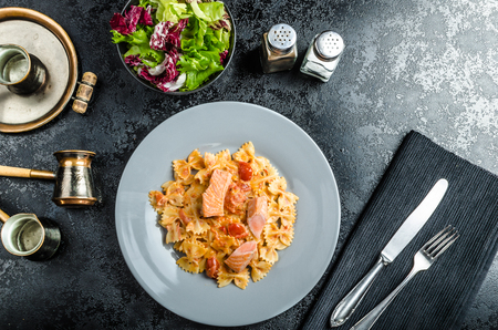 Farfalle with tomato sauce and roasted salmon, fresh endive saladの写真素材