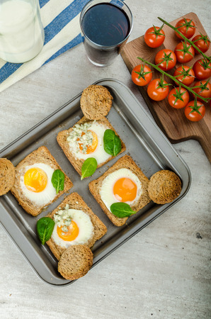 Baked Bull's-Eye Eggs on whole wheat toast with spinach and blue cheese on topの写真素材