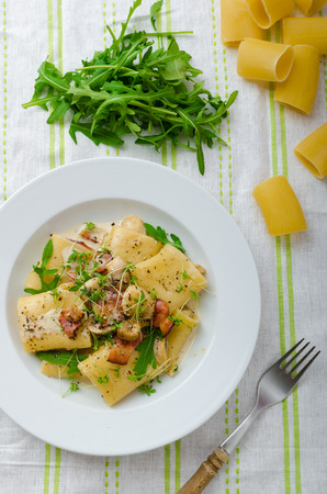 Italian rigatoni with parmesan cheese, parma ham and mushrooms, arugula and microgreens sprinkledの写真素材