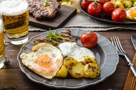 Grilled pork meat with beer, garlic dip, roasted potatoes, tomatoes and fried eggの写真素材