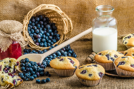Blueberry muffins milk and jam in background and basket full of blueberries