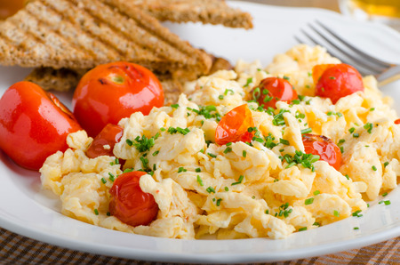 Scrambled eggs with baked tomatoes and chives, panini toastの写真素材