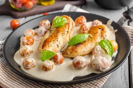 Grilled chicken breast with cream sauce and roasted tomatoesの写真素材