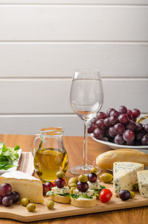 Delicious blue cheese with olives, grapes and salad, behind wine, olive oil, baquettesの写真素材