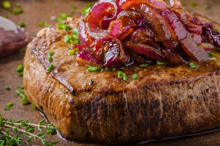 Delicious beef steak with pepper, garlic and caramelized red onion, potato pancakes behindの写真素材