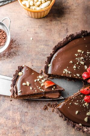 Delicious caramel chocolate tart, topped with nuts and strawberriesの写真素材
