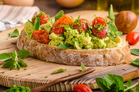 Avocado spread with tomatoes, roasted tomatoes and herbs on topの写真素材