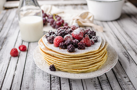 Homemade crepes with frozen berries, topped sugar, rustic wood board