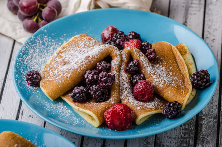 Homemade crepes with frozen berries, topped sugar, rustic wood board