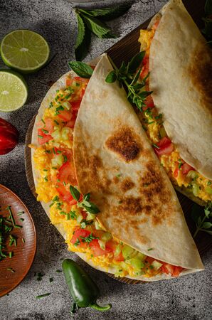 Fresh scrambled eggs with crispy tortillas, cheese, herbs and vegetableの写真素材