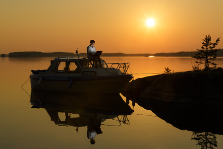 Middle aged woman with laptop by the lakeside on the boatの写真素材