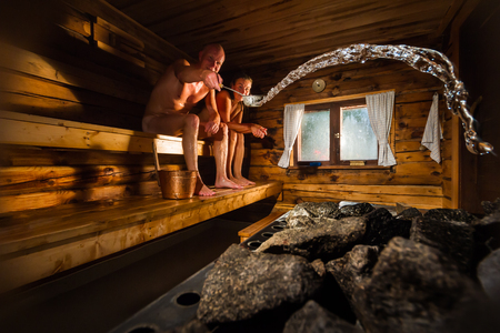 Middle aged couple in traditional wooden Finnish sauna, man throwing water to hot stoveの写真素材