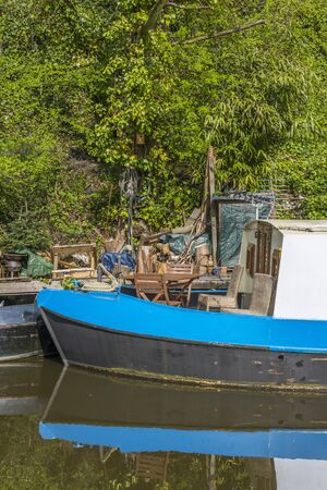 A narrowboat moored alongside some untidy garden itemsの写真素材
