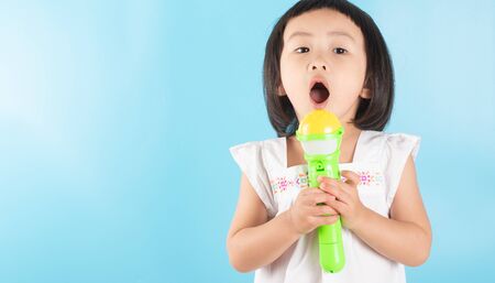 A cute Asian girl is holding a plastic microphone and singing with fun. On a blue background and copy space.の写真素材