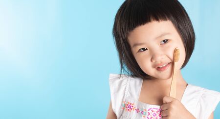 Cute Asian girl holding a toothbrush to clean her teeth on a blue background and copy space.の写真素材