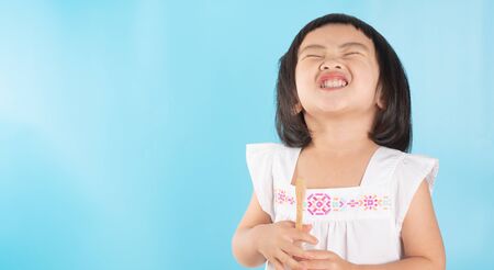 Cute Asian girl holding a toothbrush to clean her teeth on a blue background and copy space.の写真素材