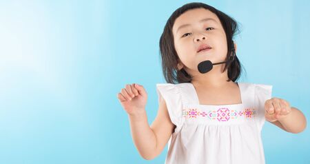 Cute Asian girl wearing voice headphones with a microphone To conduct online education during the COVID - 19 Fever Infection on a blue background and copy space.の写真素材