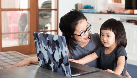 An Asian girl is learning online lessons from a notebook computer with her mother, which may be new normal in the future. To prevent infection during the Covid-19 epidemic.の写真素材