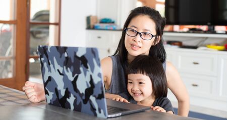An Asian girl is learning online lessons from a notebook computer with her mother, which may be new normal in the future. To prevent infection during the Covid-19 epidemic.の写真素材