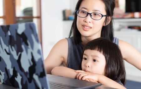 An Asian girl is learning online lessons from a notebook computer with her mother, which may be new normal in the future. To prevent infection during the Covid-19 epidemic.の写真素材