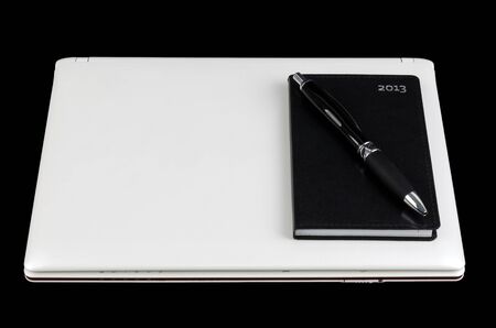White laptop with pocket calendar and pen isolated on black backgroundの写真素材