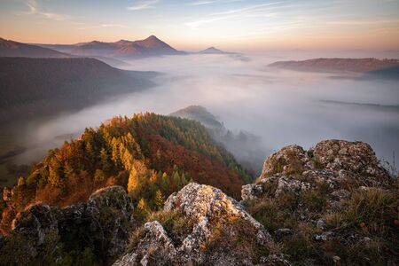 Fog in valley between mountains, sun hitting rocks and colorful leaves on trees, Slovakiaの写真素材