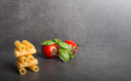 Raw Italian pasta with tomatoes an basil on a stone table front viewの写真素材