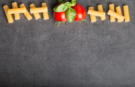 Raw Italian pasta with tomatoes an basil on a stone table top viewの写真素材