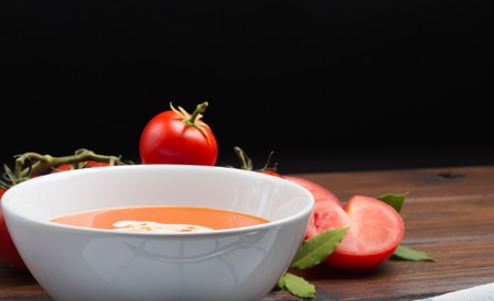 front view of fresh tomato soup on a wooden table with a black backgroundの写真素材