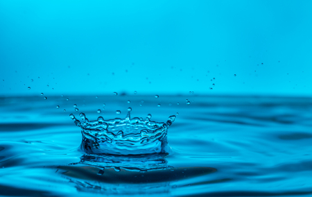 single blue drop of water hitting al large body of water and forming a crownの写真素材