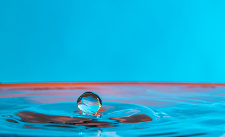 close up of a water drop falling and impacting on a body of water on a blue backgroundの写真素材