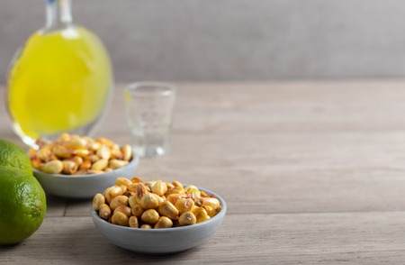 Roasted salted corn in a bowl with lemon, avocado and a bottle of liquor